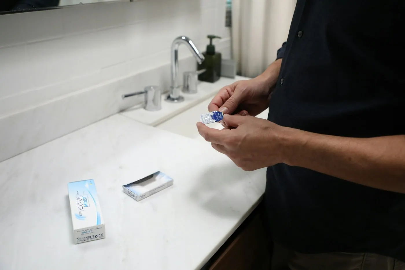 Person holding a contact lens at a bathroom counter
