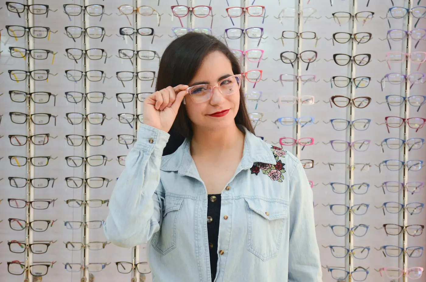 Woman trying on eyeglass frames in front of an optical display